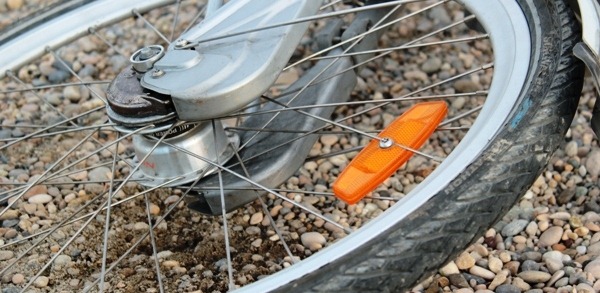 A wheel from a bike shown on the ground next to some pebbles