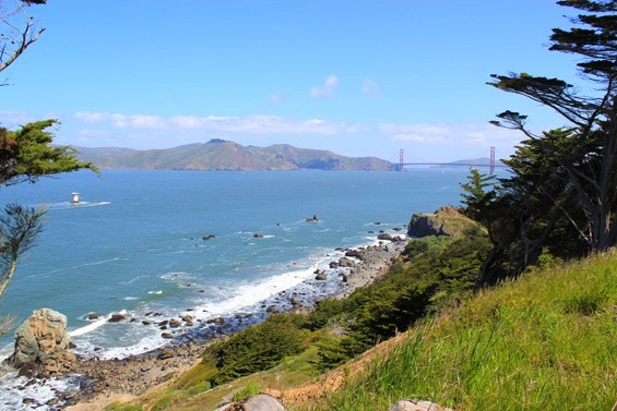 View of Golden Gate Bridge as well as the beautiful blue coastline with waves crashing into the rocks below