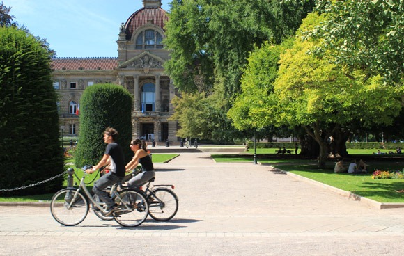 Two cyclists pedal next to the Palais du Rhin